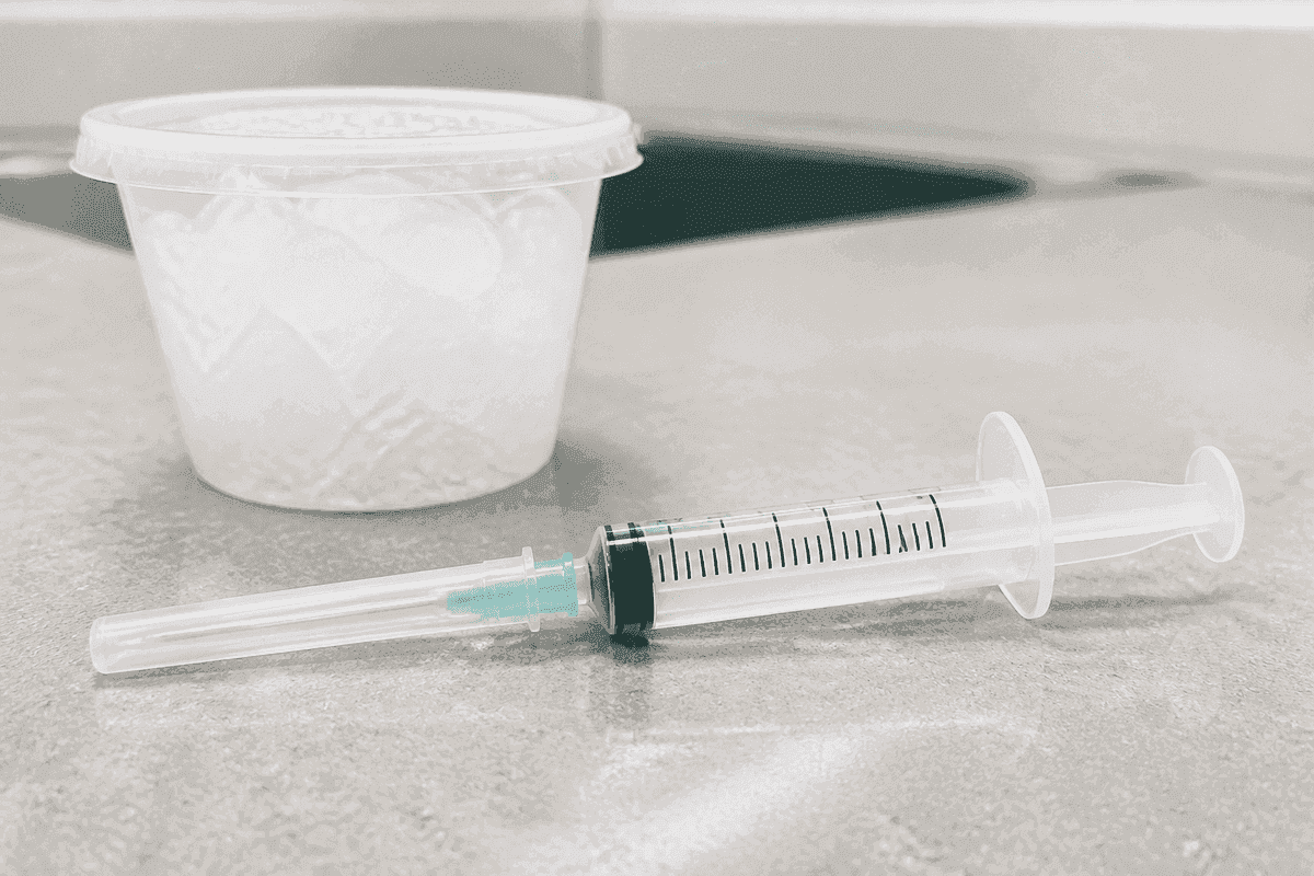 ABG syringe with cap staged beside a cup of ice for transport.